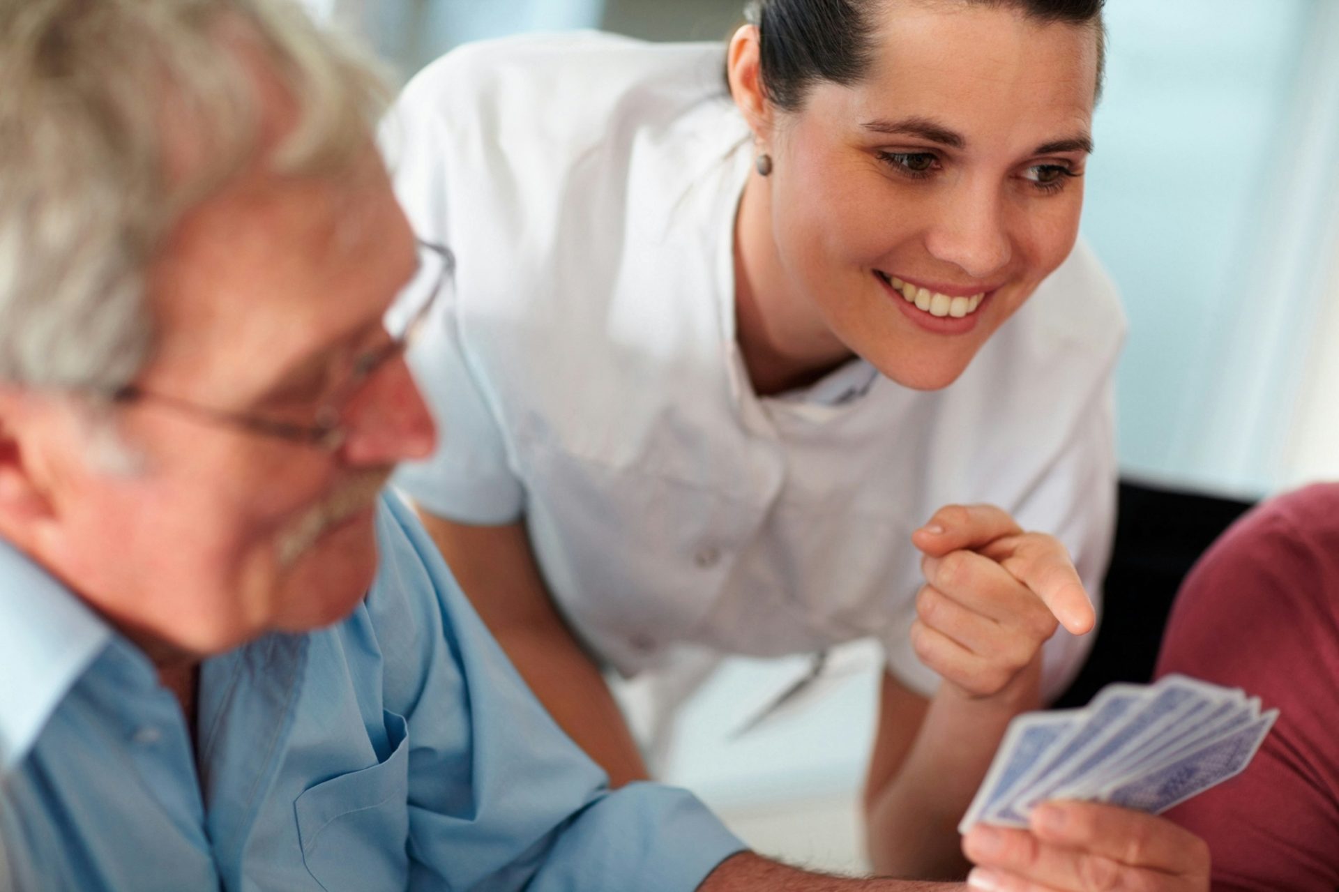 A smiling nurse plays cards with an older man.