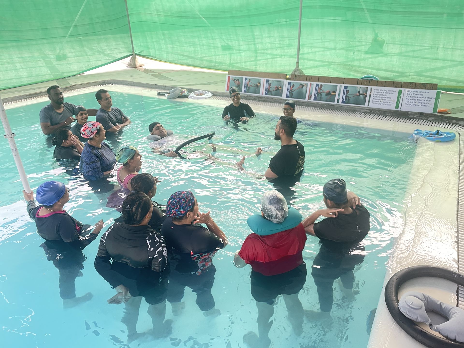 A group of therapists practice in a pool, several supporting partners who float on ring floats.