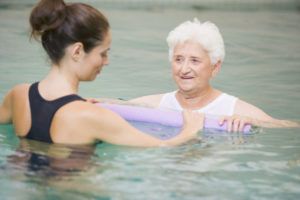 A therapist and an older woman hold a foam noodle together in the pool.