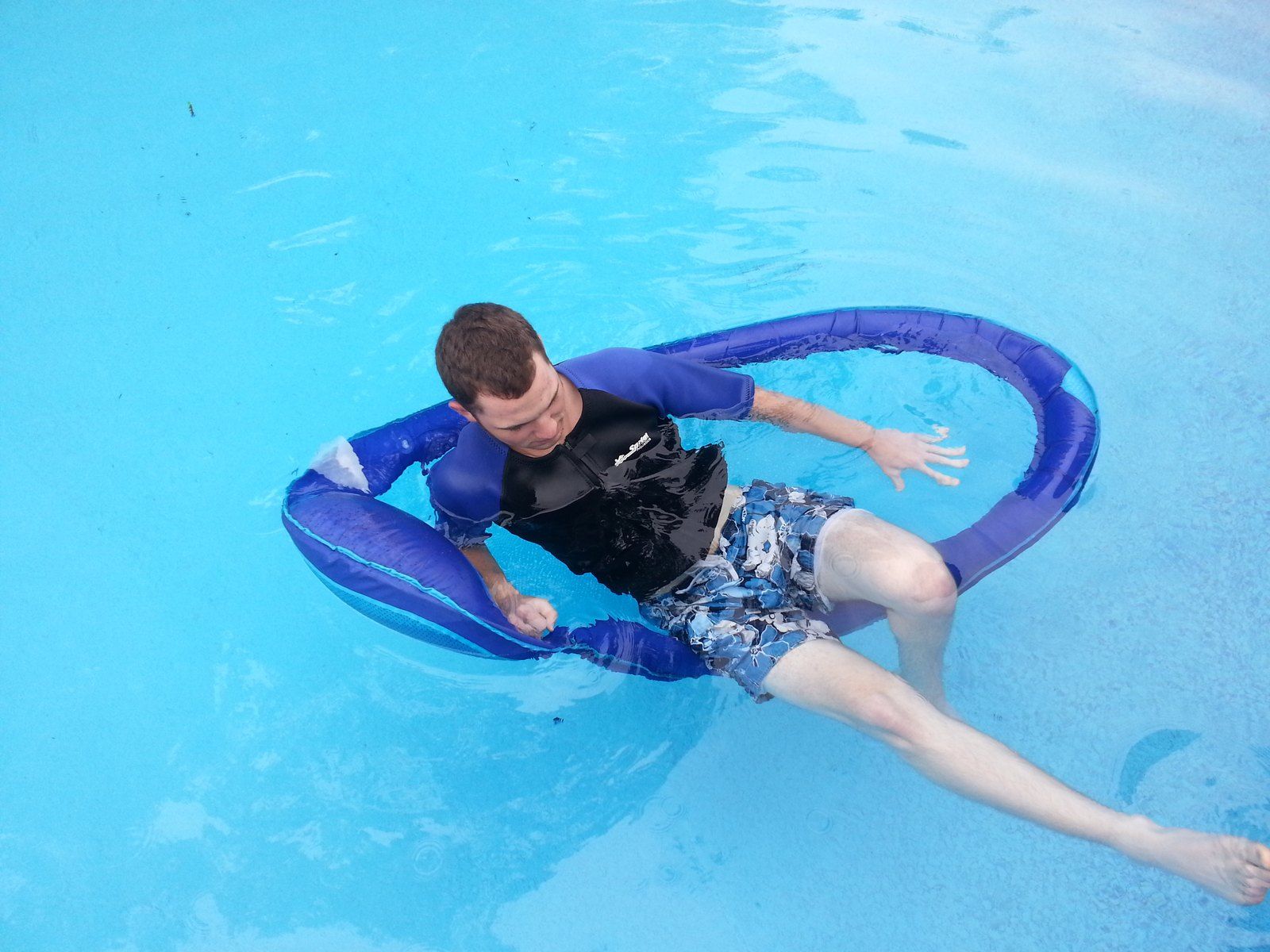 A man reclines on a blue float lounger in a pool.