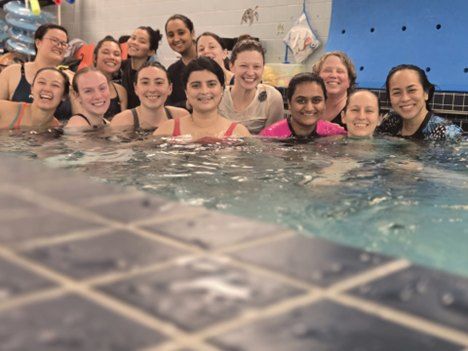 A group of women smiles at the camera from a pool.