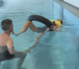 A therapist in the pool guides a client who floats on a ring.