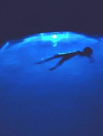 A swimmer is silhouetted in deep blue water.