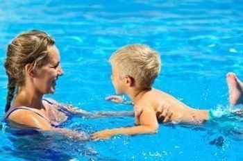 A woman and a young boy face each other while swimming in the pool.