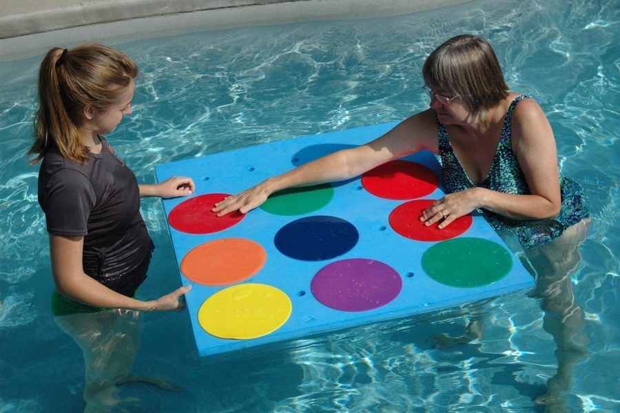 Two clinicians stand on either side of a floating mat of colored circles in the pool, practicing a hands-on activity