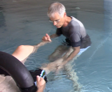 A therapist guides a client's leg pattern while the client floats on rings.