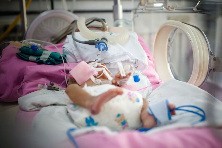 A newborn lies in a hospital crib in a neonatal unit.