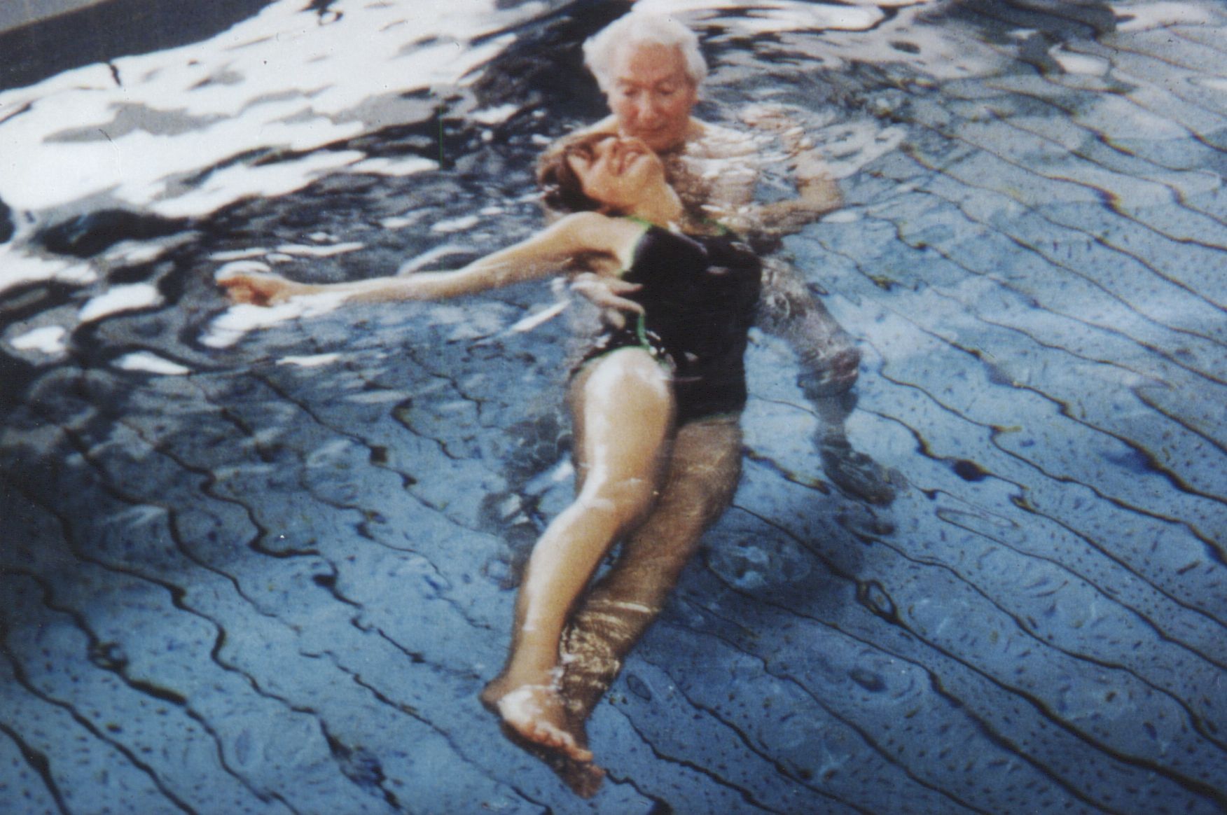 A woman floats upright in dark open water, arms out to her sides.
