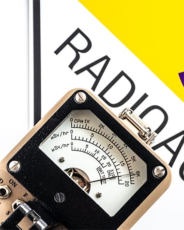 Analog radiation detector showing a reading, placed on a sign with the word “RADIOACTIVE” partially visible in bold letters.
