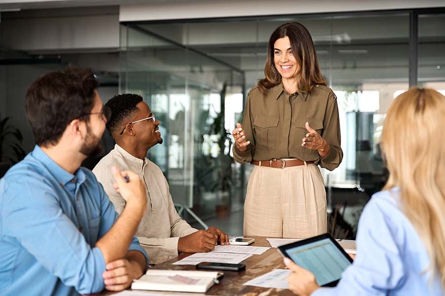nonprofit manager standing at end of table talking with confidence hand gestures to smiling team