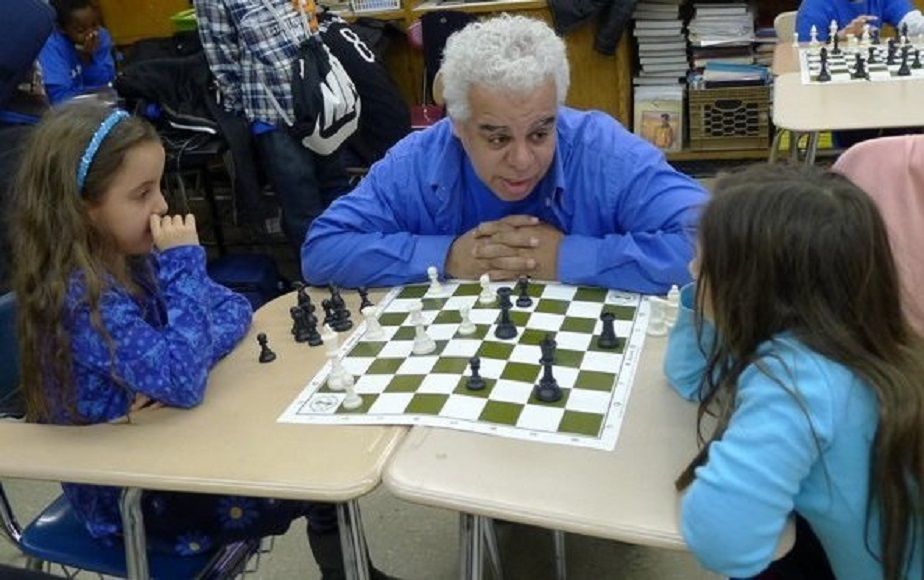 National Master Ernest Colding teach 2 young girls how to play chess.