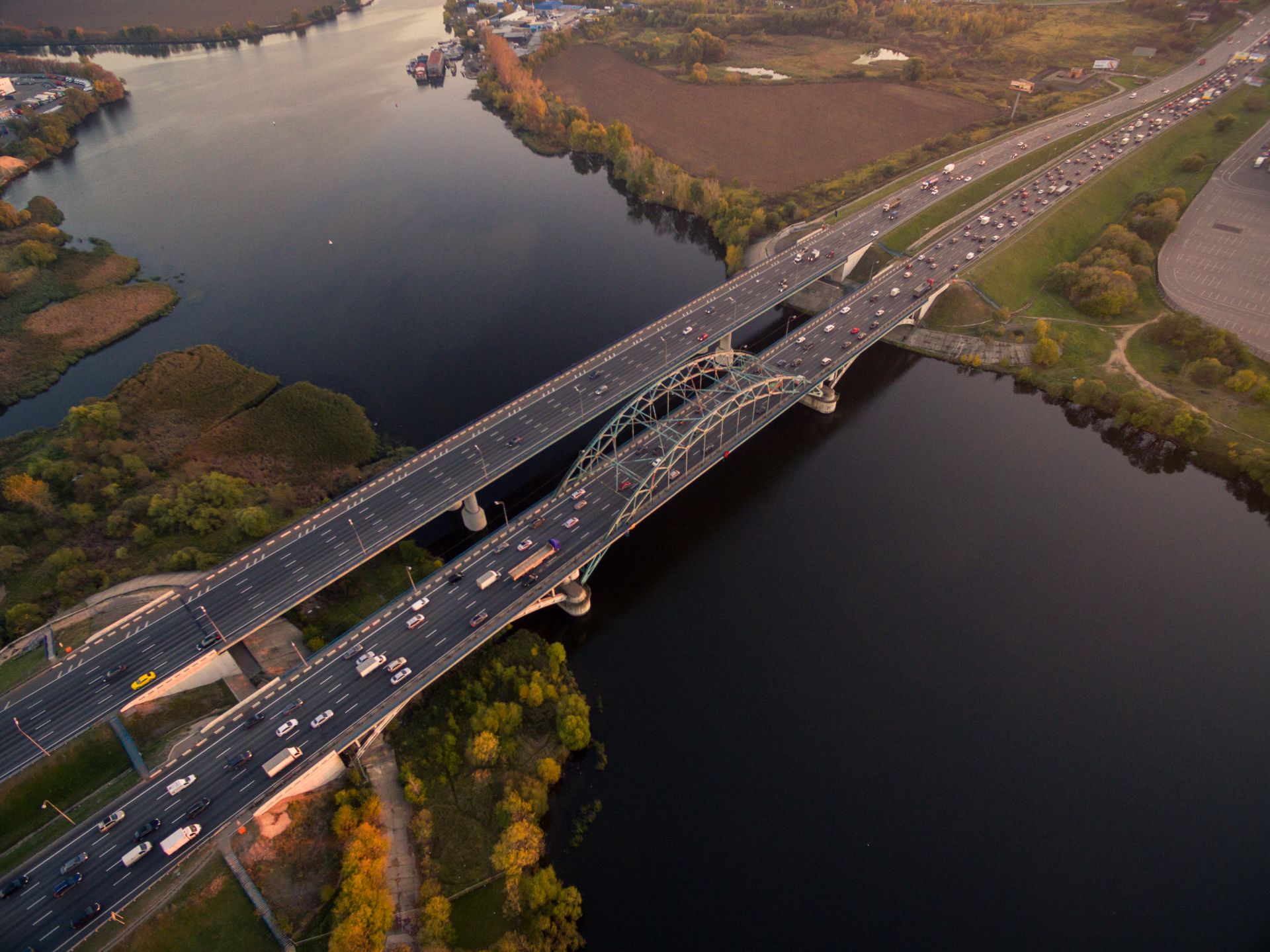 Aerial view at dusk of a multi-lane arch bridge crossing a wide river, traffic flowing on both carriageways