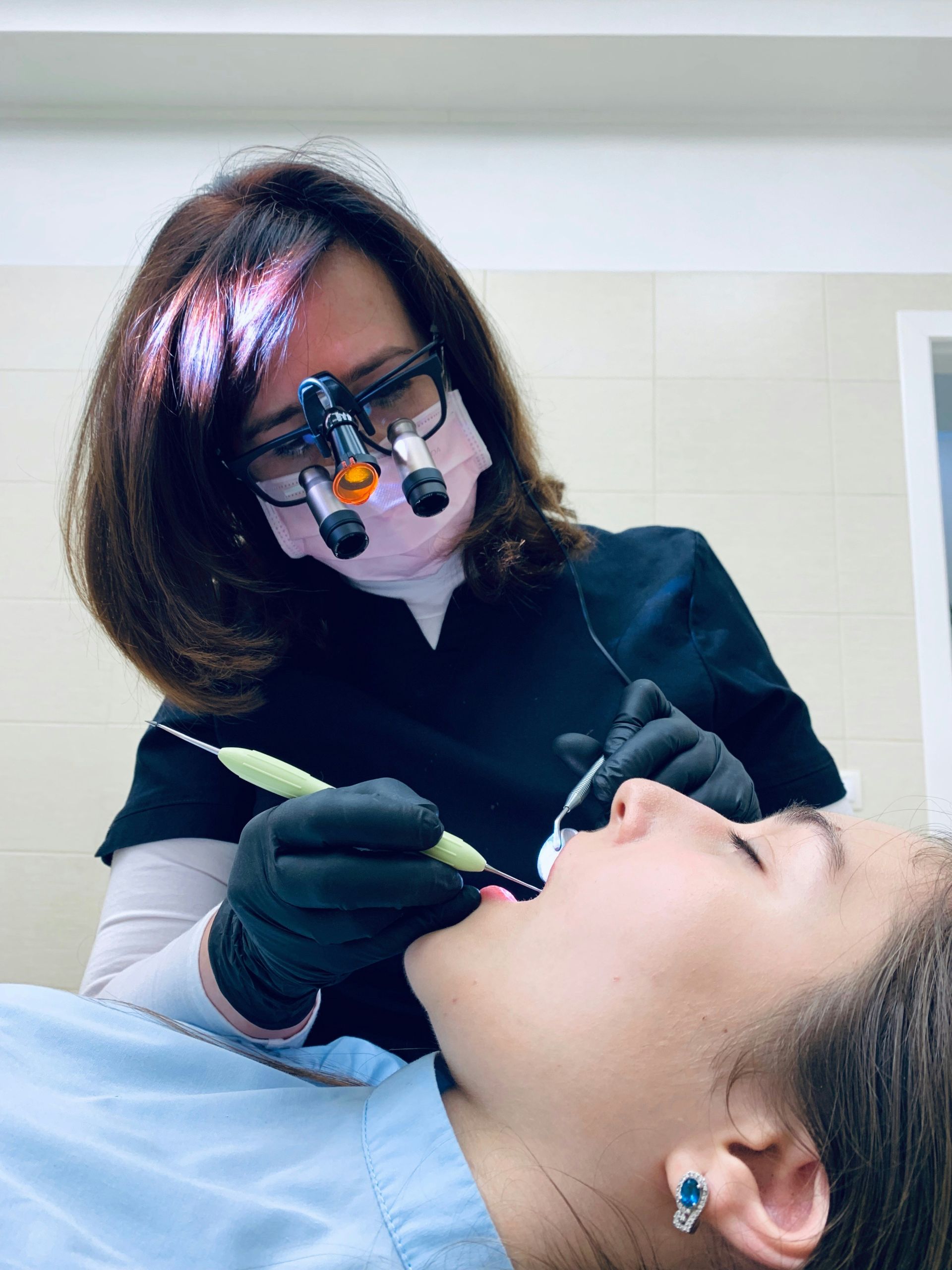 a woman dental provider is scaling the teeth of a young woman