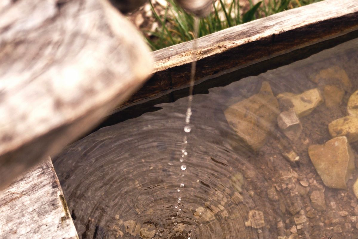 Water falling from a wooden spout into a stone trough, rings spreading out