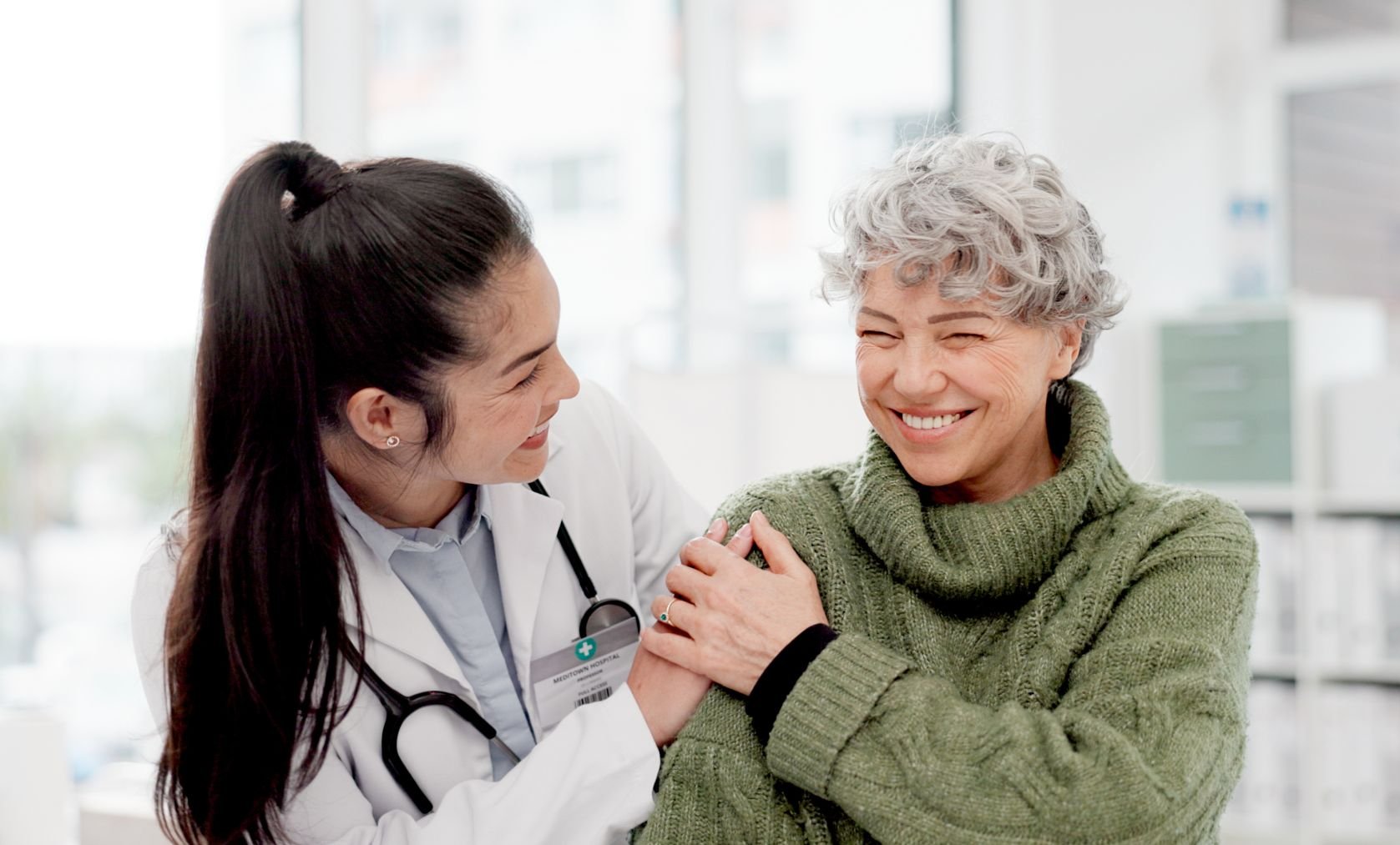 Female physician holding shoulder of elderly female patient, both smiling and comfortable