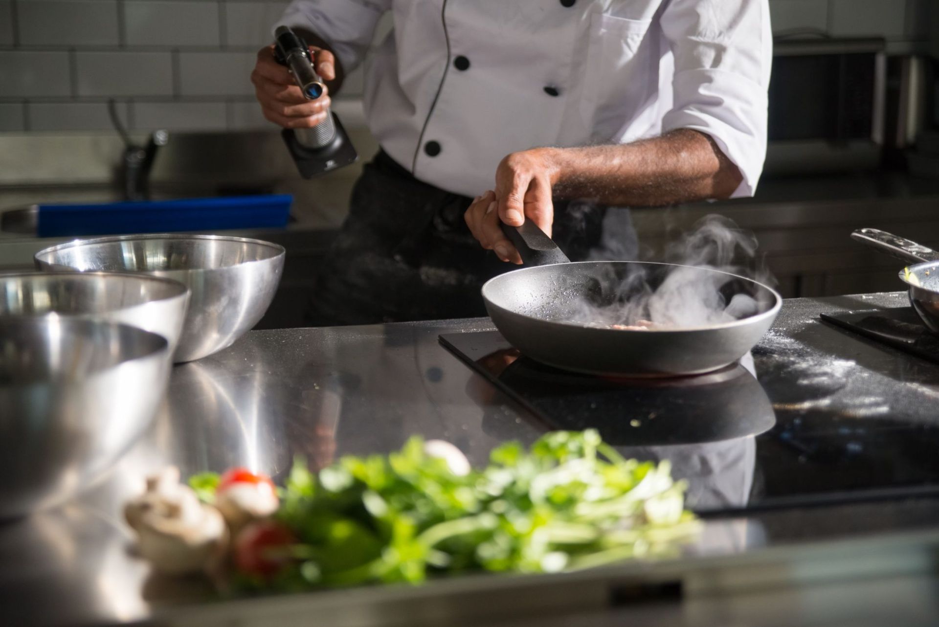 A chef in whites cooking over a steaming pan with fresh ingredients