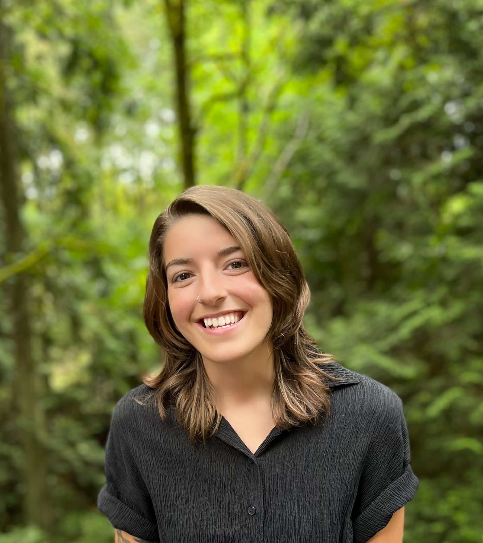 Image of a smiling woman in a black shirt with brown hair standing in the woods