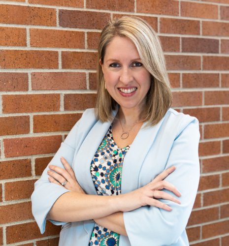 Image of Melissa Kimmerling, she is a caucasian female with blonde medium length hair, blue eyes, black blazer with a blue shirt on with a black and yellow faded background. 