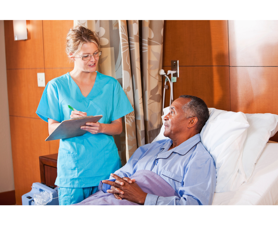 female with blonde hair and light blue scrubs holding clip board and looking down at African American man in hospital bed in blue pajamas