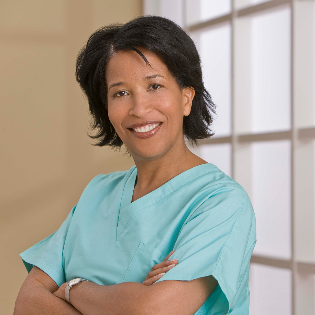 Woman with dark skin, dark hair in mint green medical scrub with arms crossed 