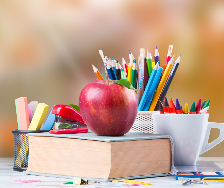 Image of a book with an apple on it, with 3 cups holding writing utensils