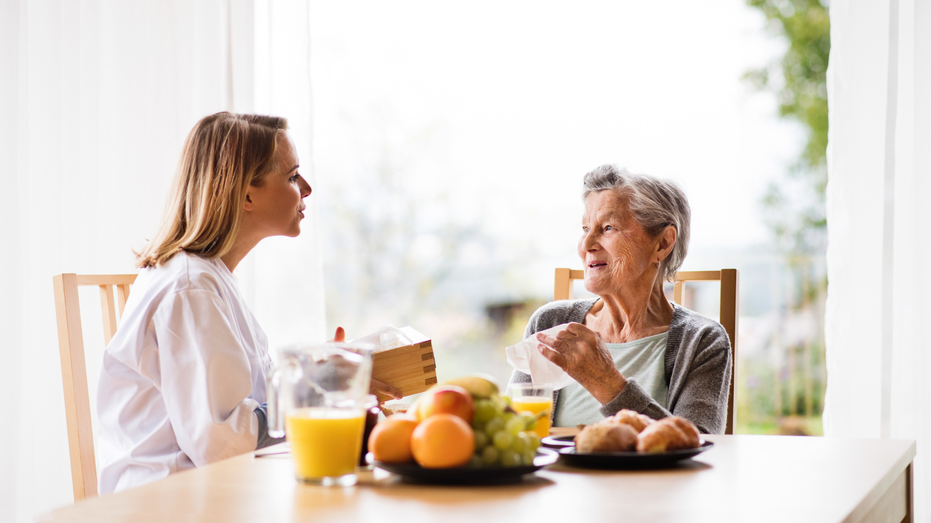 photo of an older woman sitting at table with a younger woman in a white lab coat