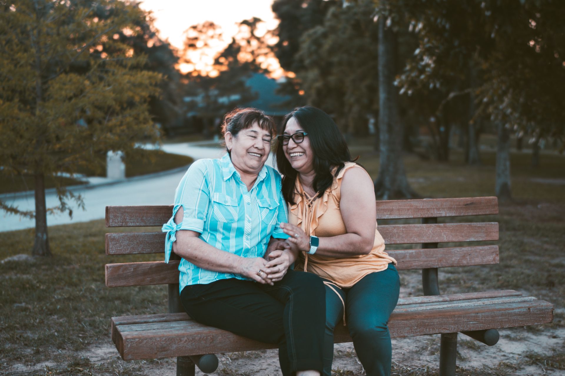 Two intergenerational women sitting close together on a park bench