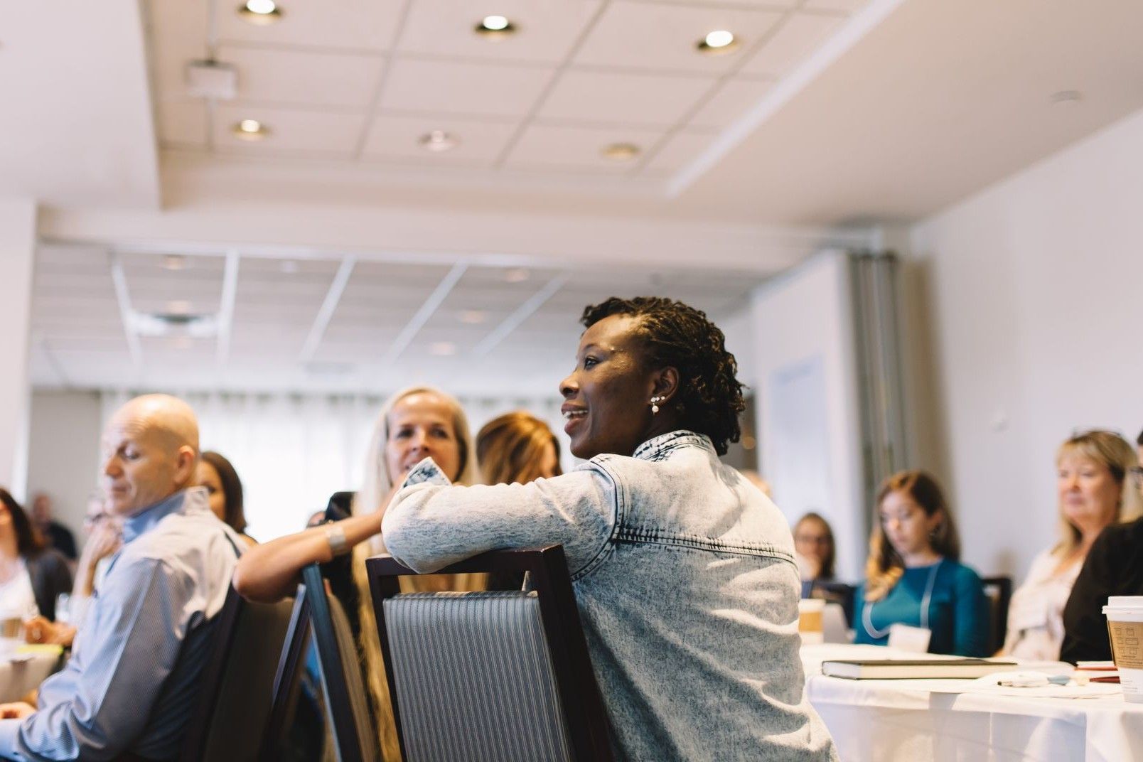 Woman leaning her arm on the back of a chair, smiling while listening during a workshop