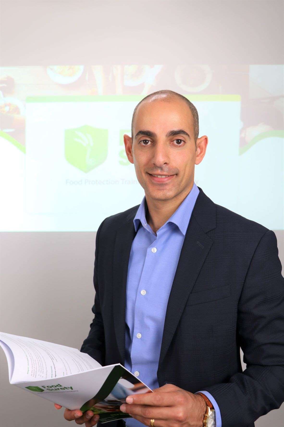 A portrait photo of food safety trainer -Ray Haddad from food surety limited while holding a HACCP training manual in his hands.