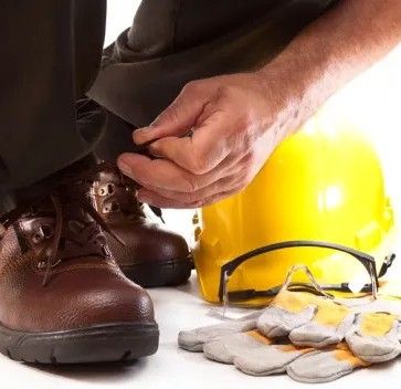 Worker adjusting safety gear beside boots, gloves, hard hat, and eye protection to emphasize PPE use during invasive species control on the ROW.