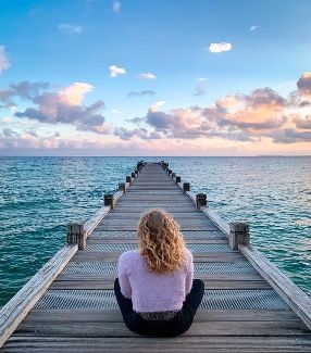 Meditation am Meer: Frau sitzt auf Holzsteg und beobachtet Sonnenuntergang