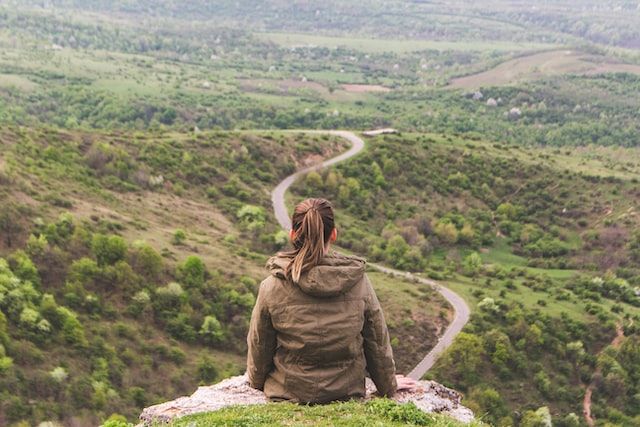 jeune femme se tenant assise sur un rocher en hauteur et regardant une route au loin