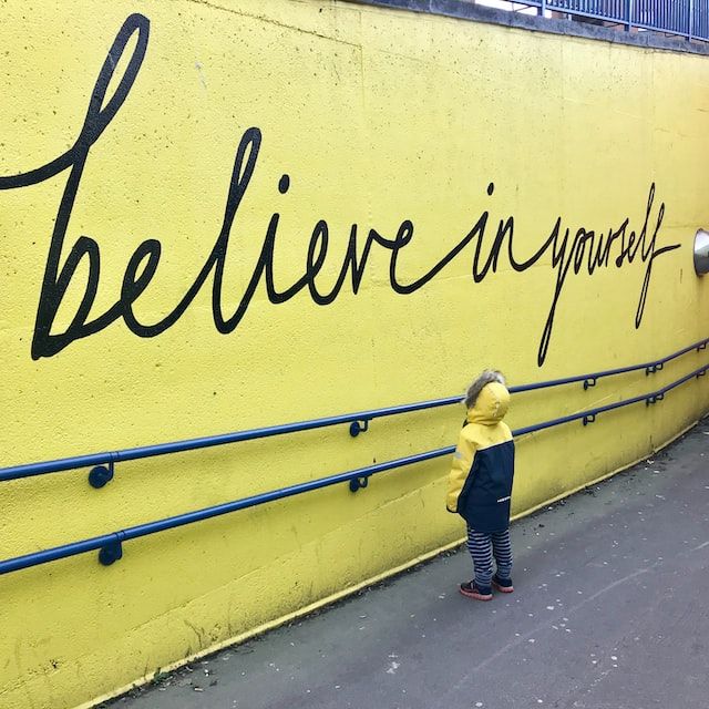 enfant regardant la phrase believe in yourself sur un mur jaune