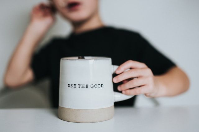 enfant tenant une tasse avec inscription "see the good"