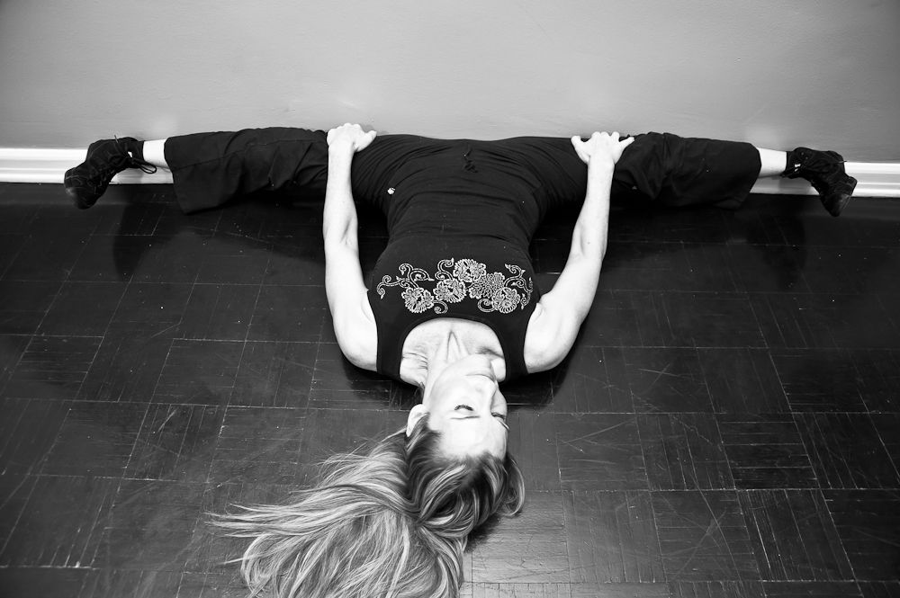 Stacey lying on floor against wall legs out in full middle splits straddle stretch in Kung Fu Magazine