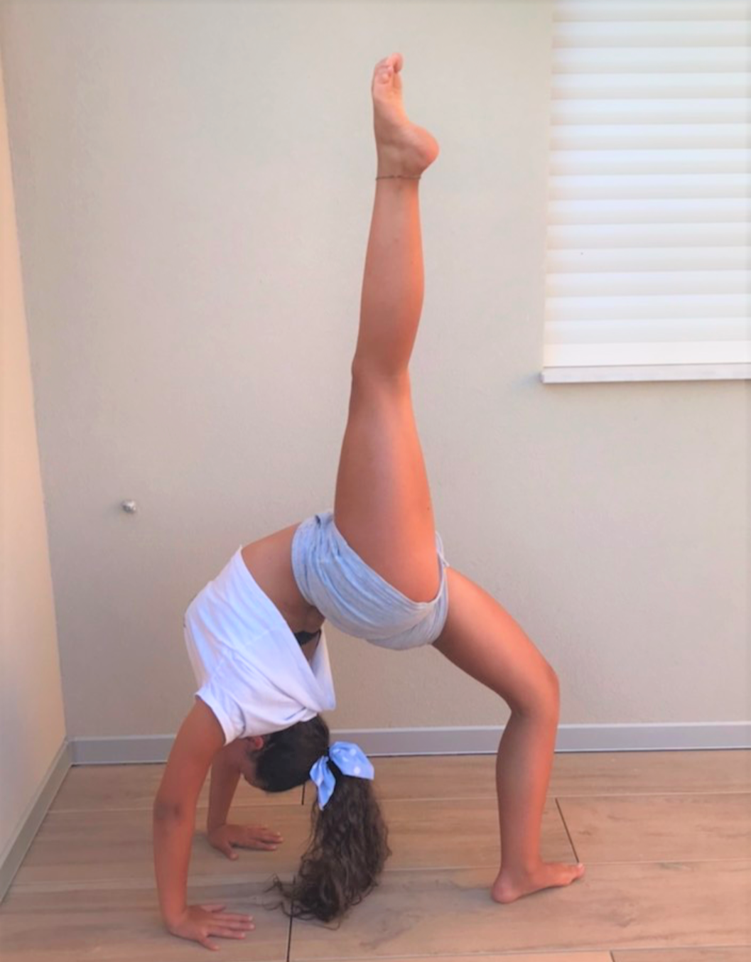 Girl in backbend with one leg extended straight up pointing at ceiling