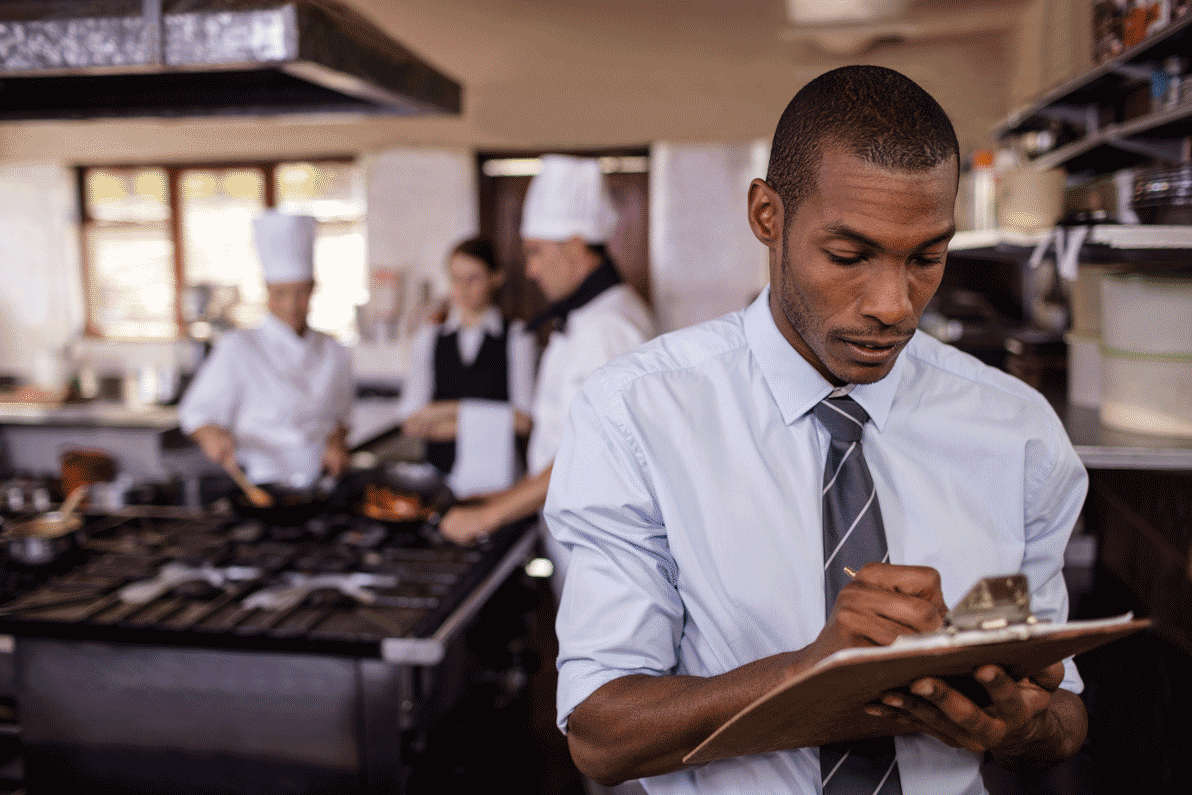 Restaurant manager writing on clipboard in restaurant kitchen