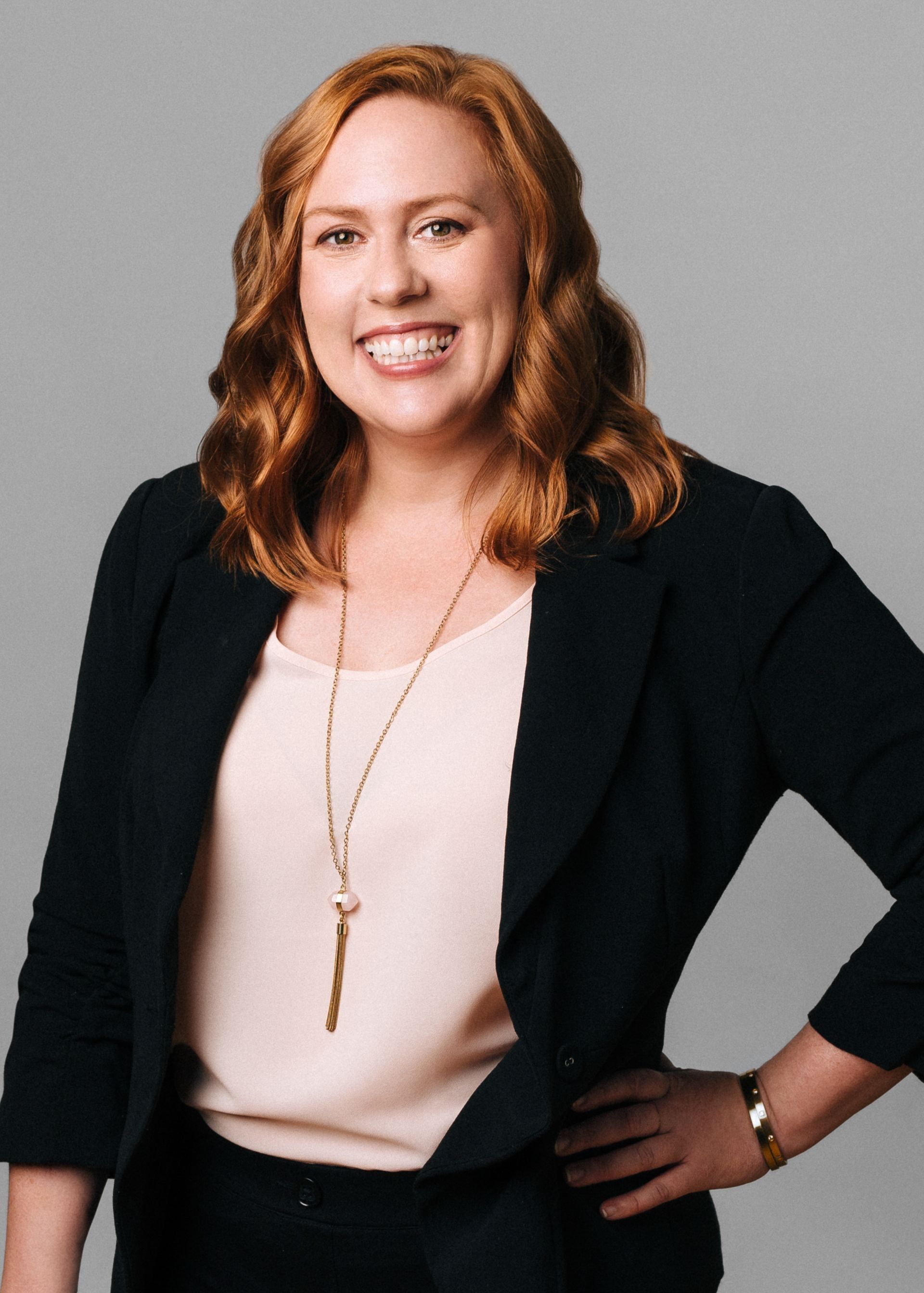 Leadership Coach, Aleta Maxwell, standing with hand on hip and smiling. Wearing a blush shirt and black suit jacket with jewelery