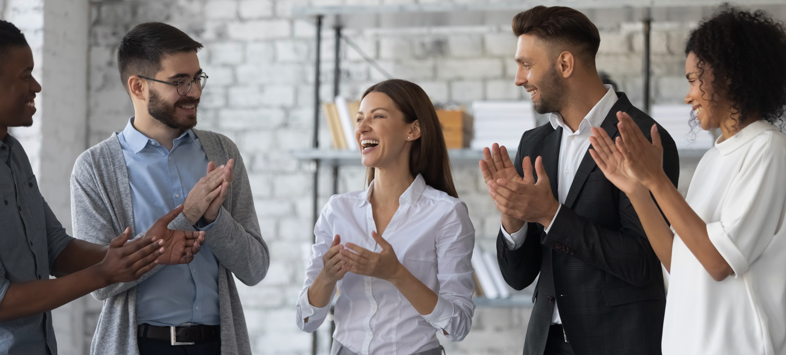 Three business people clapping for female colleague in their workplace