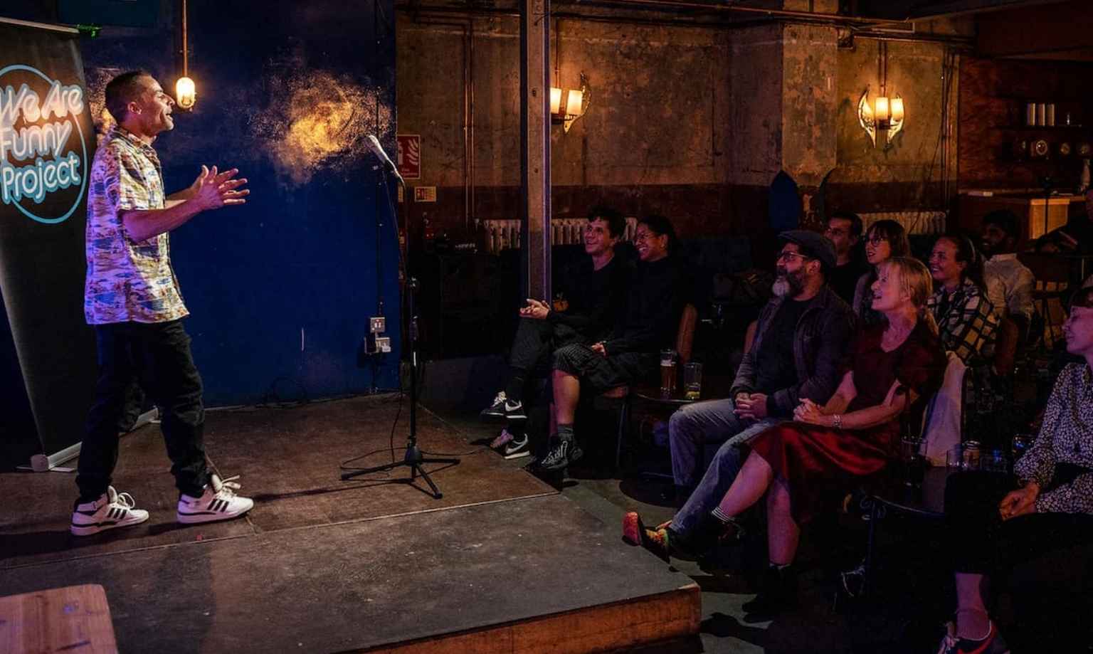 Alfie Noakes on a stage addressing a crowd of people, many of whom are laughing and smiling