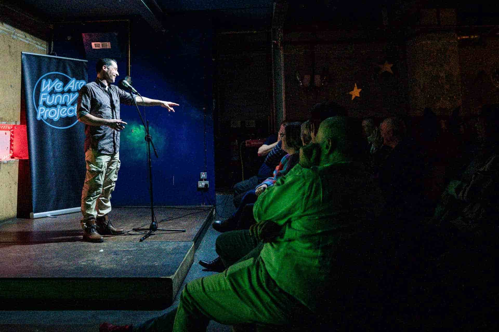 Alfie Noakes smiling on a stage in front of a crowd and pointing to a laughing audience member
