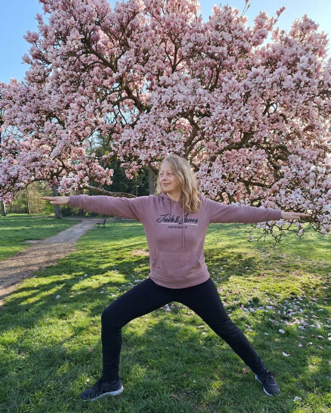 Mila Rivault en posture debout, bras ouverts, devant un magnolia en fleurs